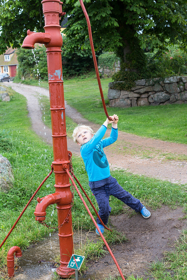 5 year old boy pumping water with a traditional water pump, Baltic sea, MR, Bornholm, Svaneke, Denmark, Europe