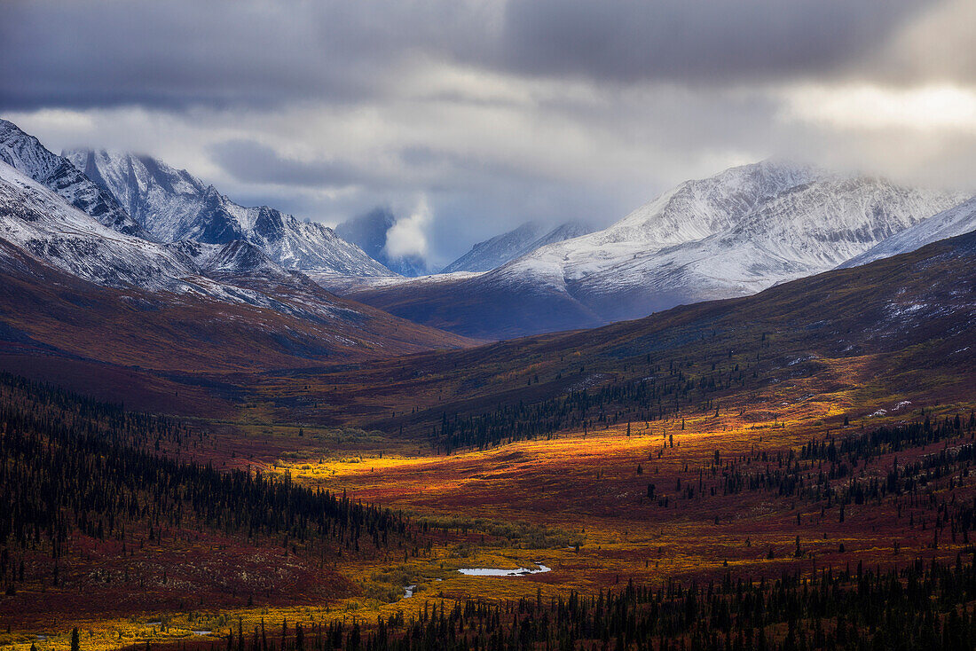 Storm clouds part allowing light to illuminate the landcape in the North Klondike Valley along the Dempster Highway in northern Yukon, Yukon, Canada