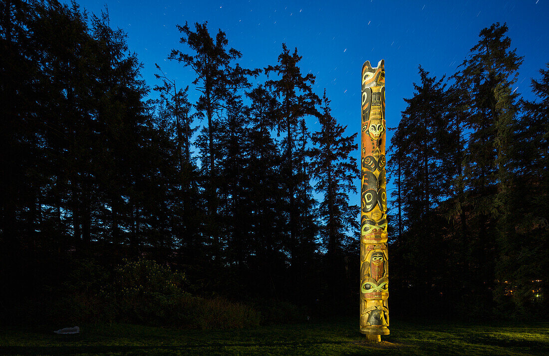 A large Totem Pole lit up at night in Sitka National Historic Park, Sitka, Southeast Alaska, USA, Summer