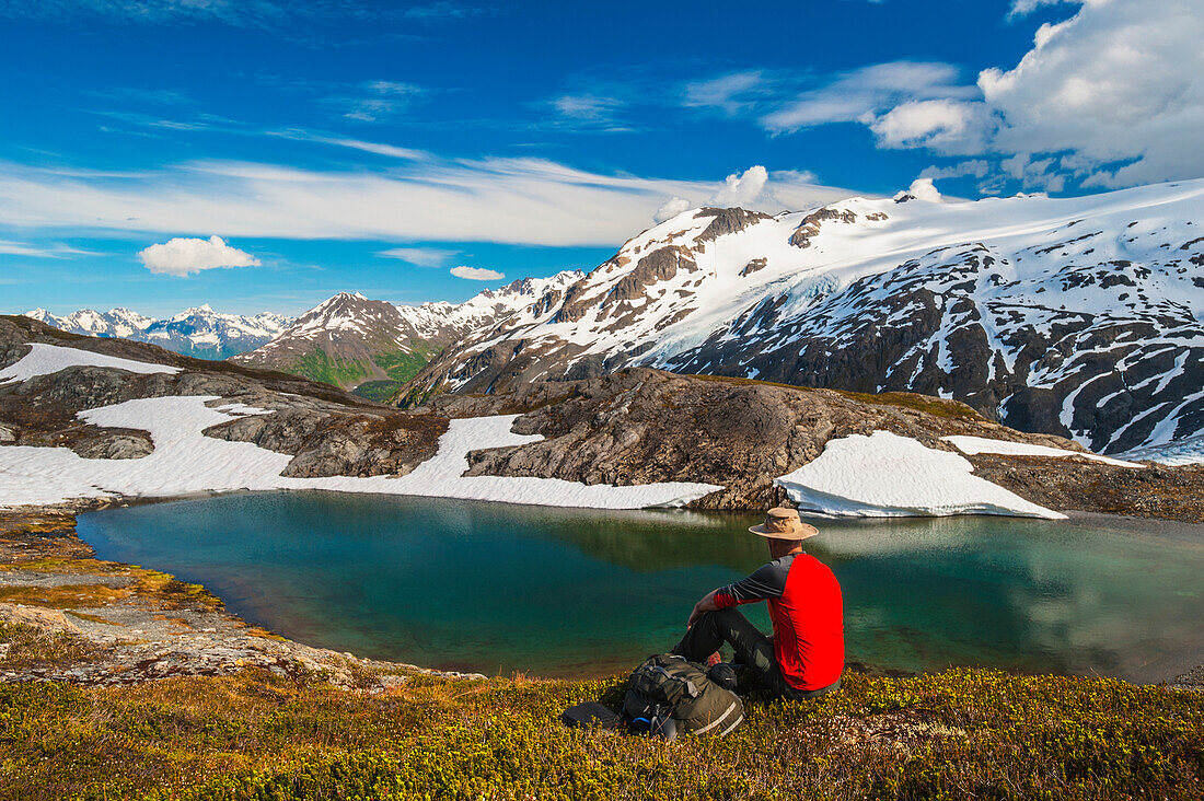 Hiker rests alongside a lake while hiking the Harding Icefield Trail, Kenai Fjords National Park, Kenai Peninsula, Southcentral Alaska