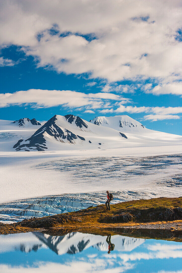 A man hiking by a lake with the Harding Icefield and the Nunatak peaks in the background, Kenai Fjords National Park, Southcentral Alaska