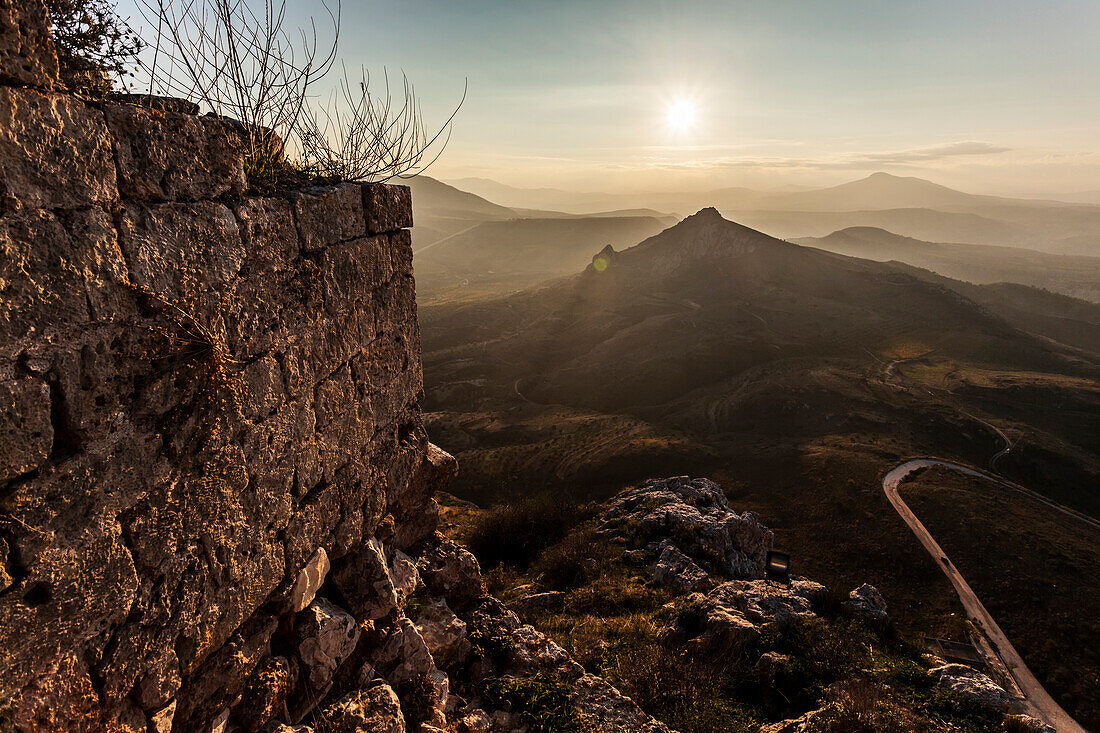 Ruins of a stone wall with a sunburst and mountains, Corinth, Greece