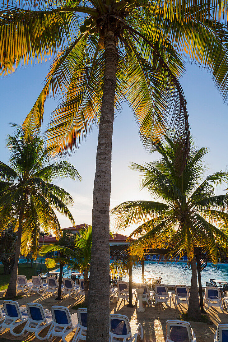 The sun sets behind palm trees outlining the pool and lounge chairs at a resort in Cuba, Varadero, Cuba