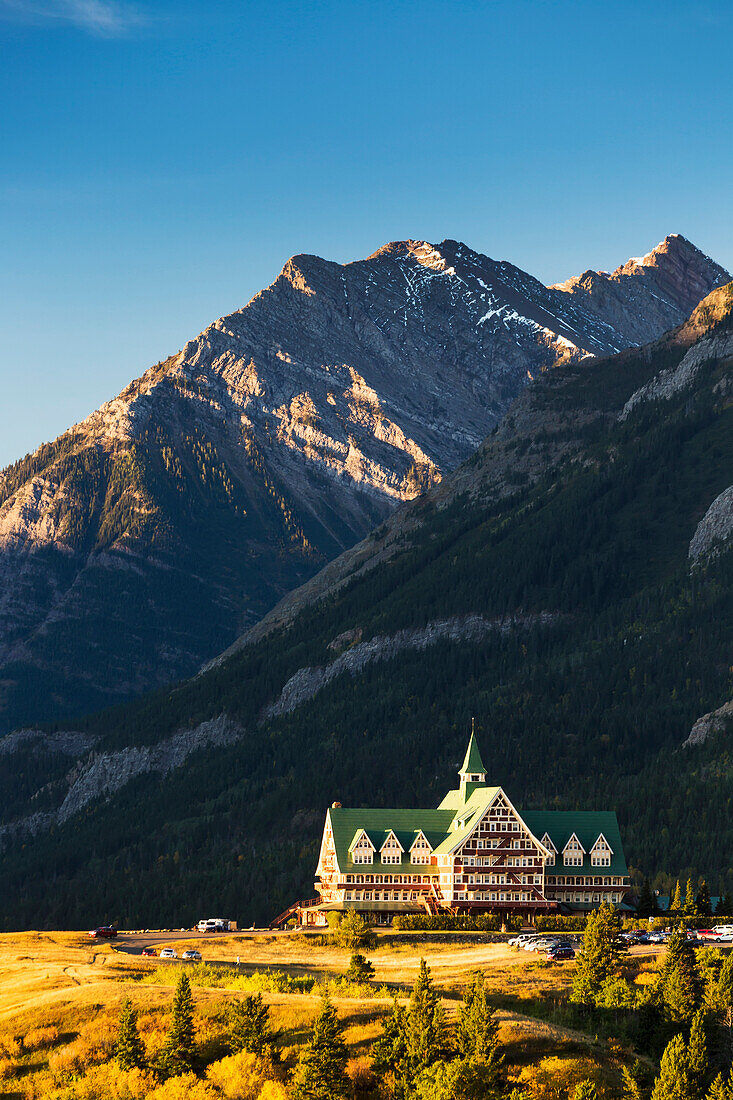 Prince of Wales hotel on a hilltop at sunrise with mountain and blue sky in the background, Waterton, Alberta, Canada