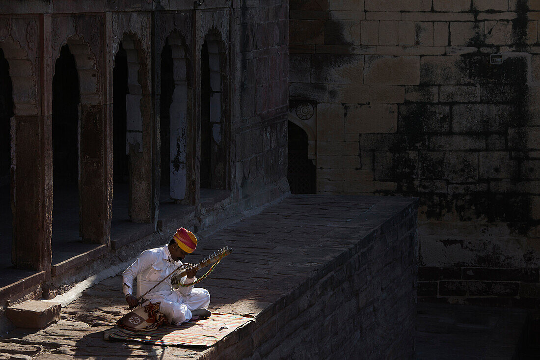 Mann spielt auf einer Esraj in den Gemäuern der Festungsanlage Meherangarh, Jodhpur, Rajasthan, Indien