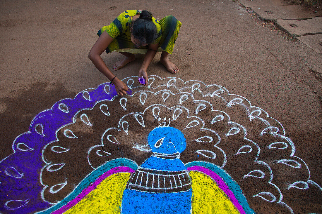 A young Indian female painting a peacock on the street in celebration of a festival, Betul Beach, Goa, India