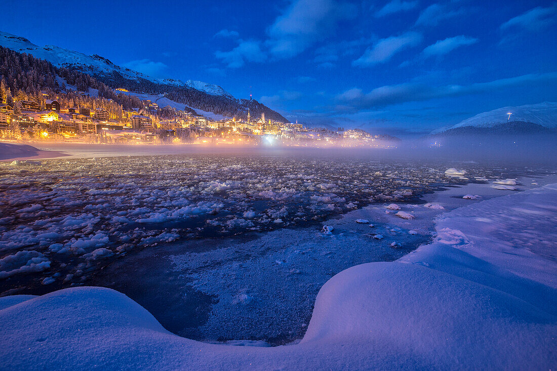 The frozen Inn river and the village of Sankt Moritz at dusk, Engadine, Canton of Grisons Graubunden, Switzerland, Europe