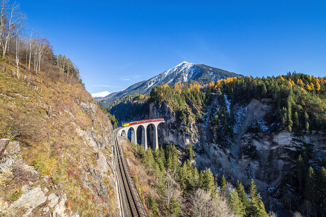 Bernina Express passes over the Landwasser Viadukt surrounded by colorful woods, Canton of Graubunden, Switzerland, Europe