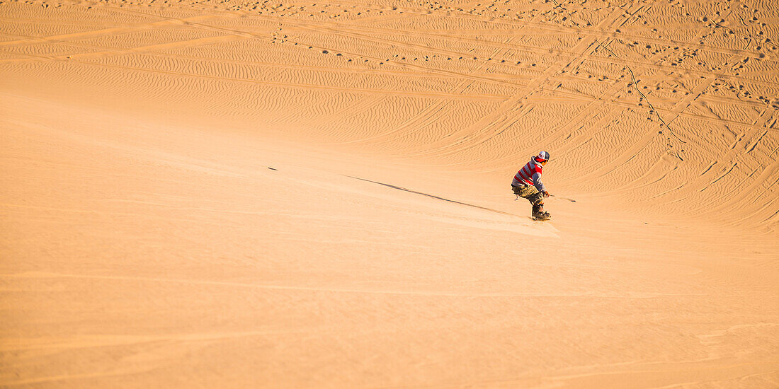 Sand boarding on dunes in the desert at Huacachina, Ica Region, Peru, South America