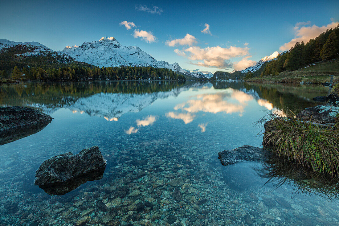 Dawn illuminates the snowy peaks reflected in the calm waters of Lake Sils, Engadine, Canton of Graubunden, Switzerland, Europe