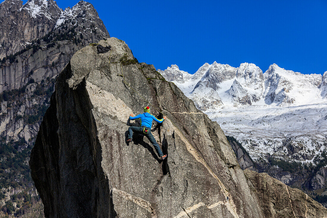 Climber on steep rock face, in the background blue sky and snowy peaks of the Alps, Masino Valley, Valtellina, Lombardy, Italy, Europe