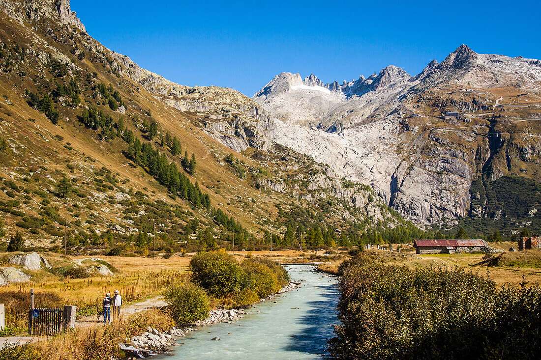 randonneurs longeant le rhone naissant a la sortie du village de gletsch avec en fond une perspective sur le glacier du rhone, source du rhone, gletsch, canton du valais, suisse