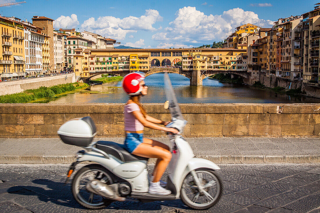 jeune femme filant sur sa vespa avec en fond le ponte vecchio le pont emblematique de florence, florence, toscane, italie, union europeenne
