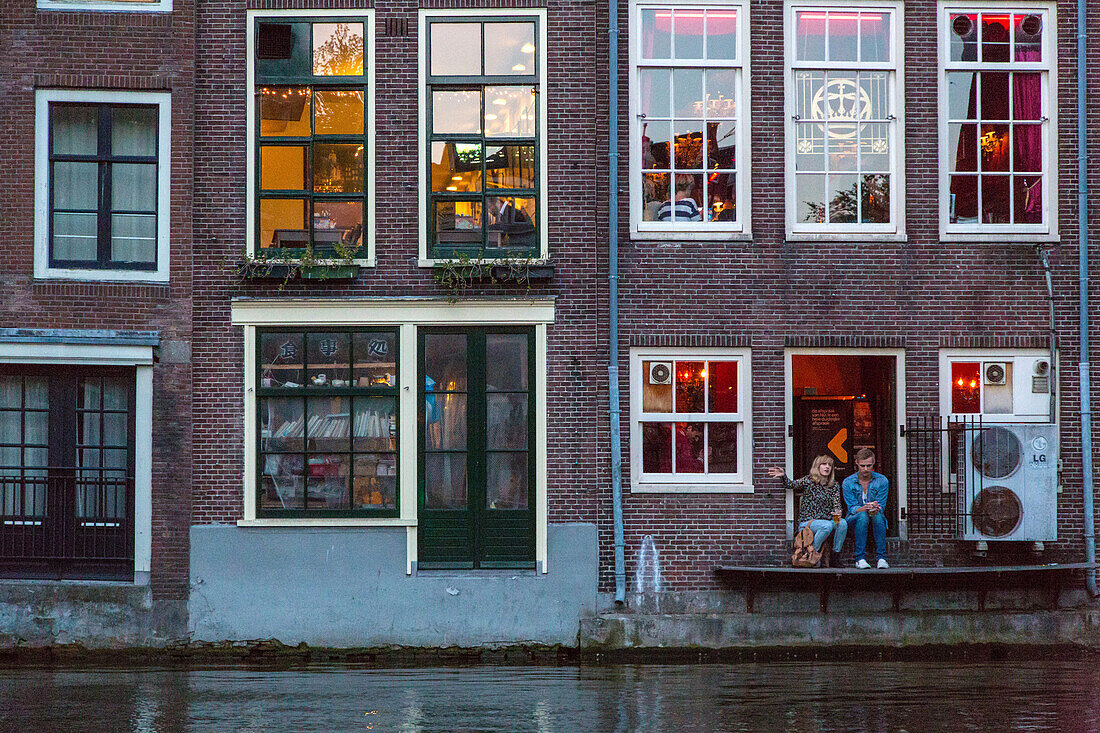 couple and houses on the water, voorburgwal canal, amsterdam, holland