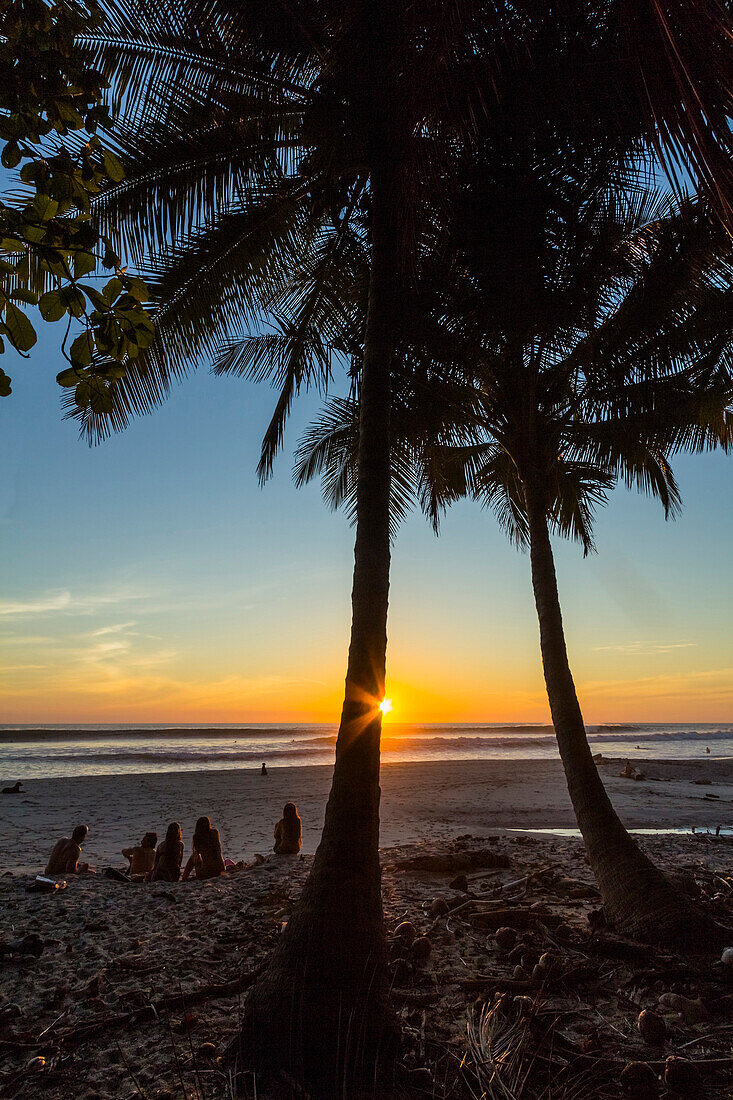 People by palm trees at sunset on Playa Hermosa beach, far south of the Nicoya Peninsula, Santa Teresa, Puntarenas, Costa Rica, Central America