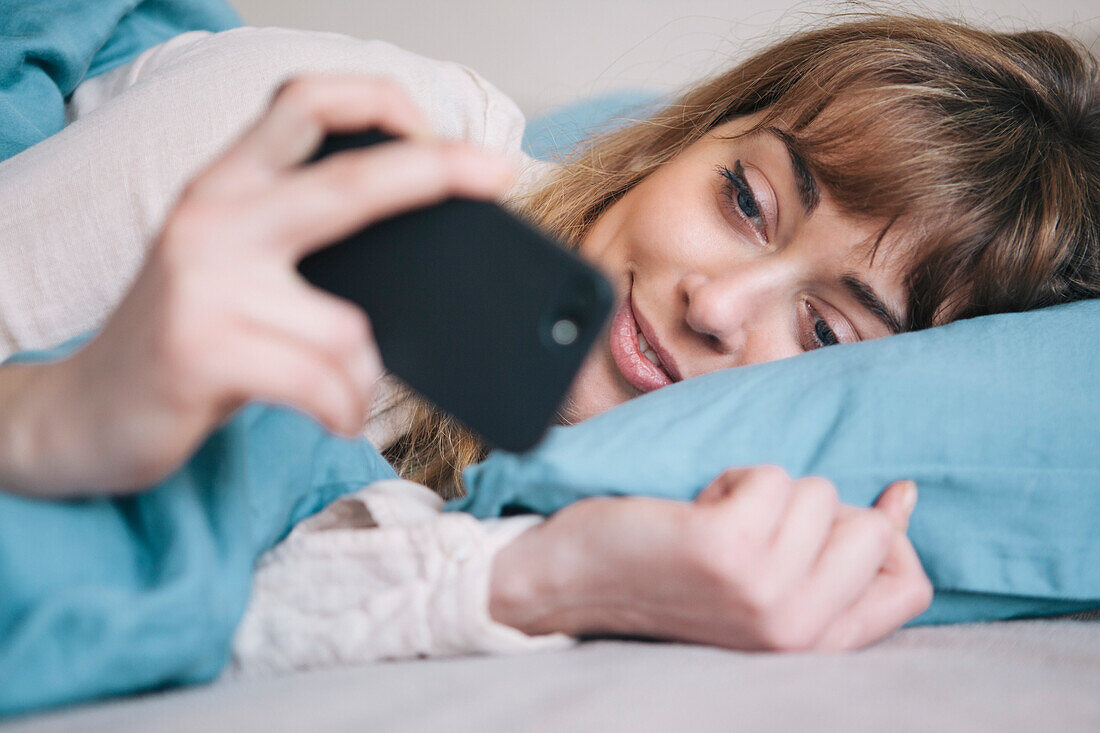 Young woman using mobile phone while relaxing in bed