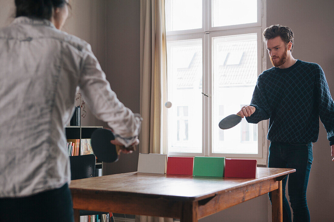 Young man playing table tennis with woman at home