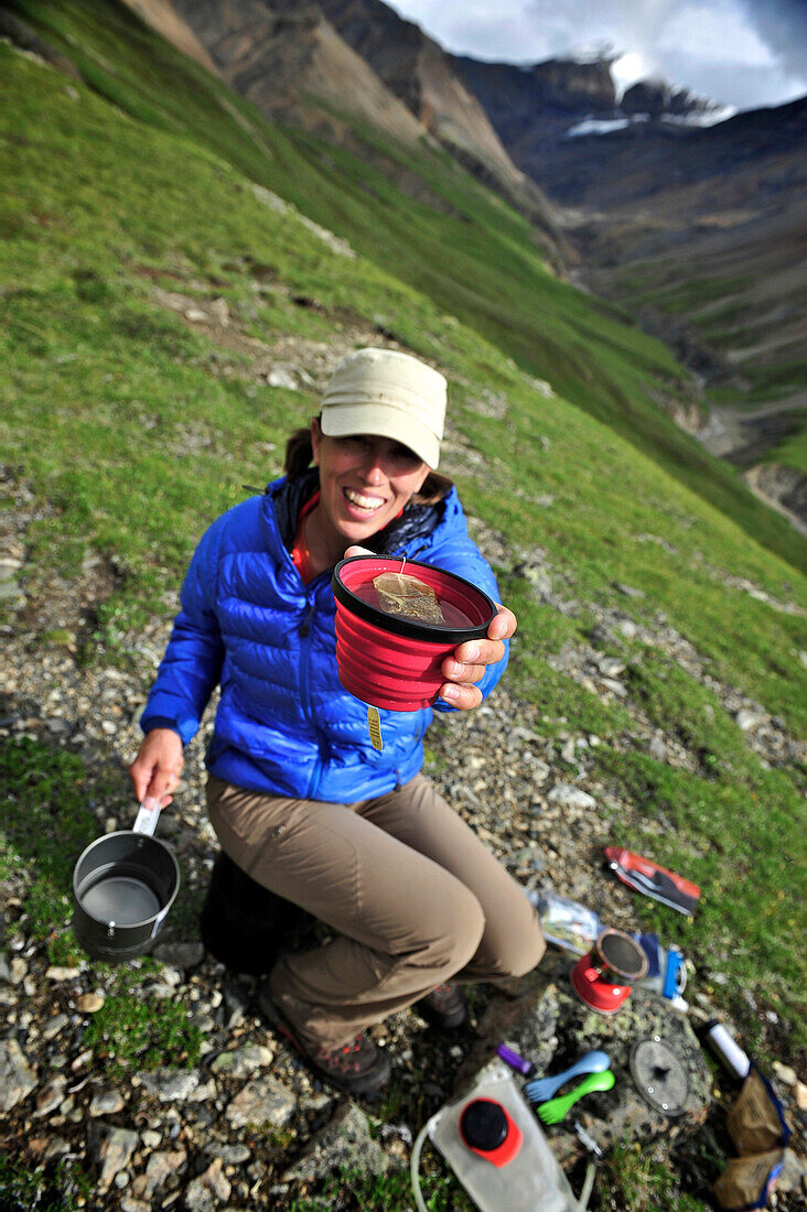 Woman backpacker prepares meal at camp above Sunrise Creek in the Thorofare River valley in Denali National Park & Preserve, Alaska July 2011. Scott Peak can be seen in the background. She is cooking dehydrated camp meals with an MSR Reactor Stove.
