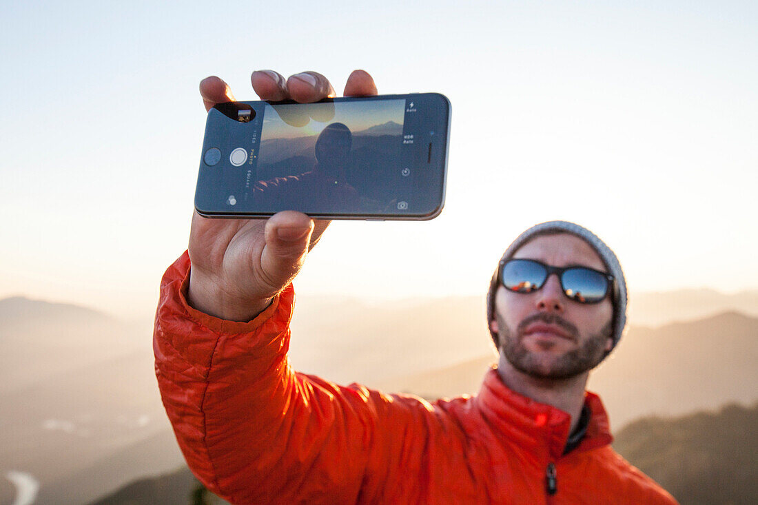 A hiker uses his smartphone to take a selfie while enjoying the outdoors.