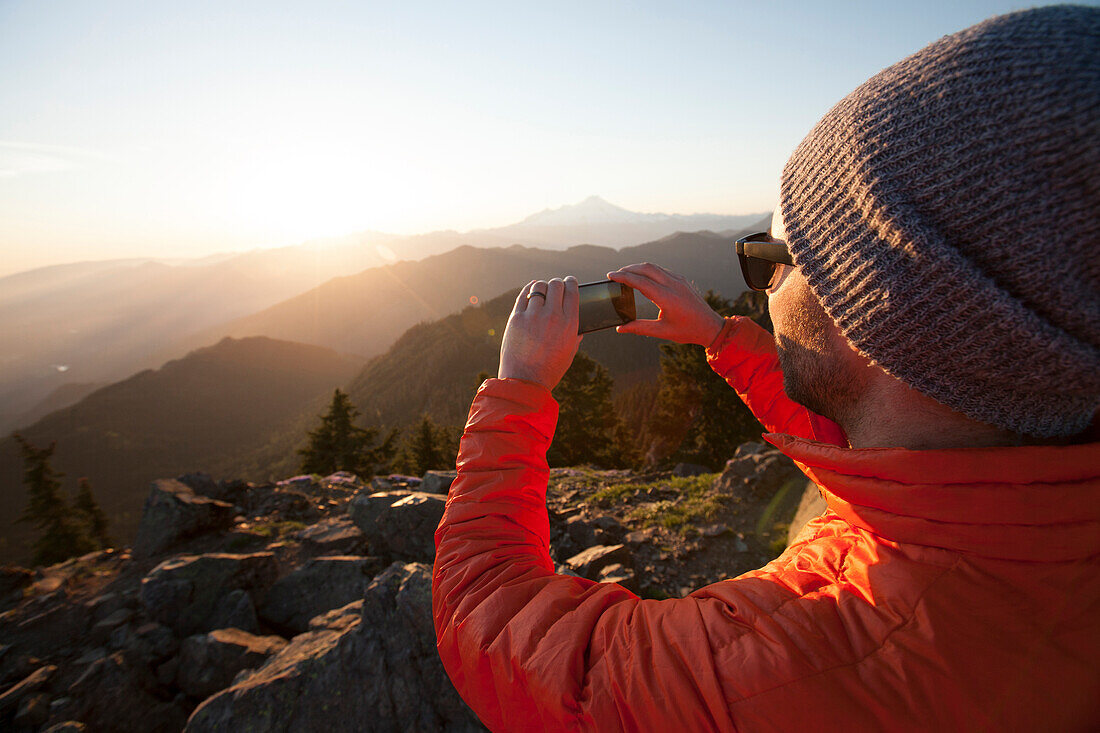 A hiker uses his smartphone to take a a picture of the view from the summit of Sauk Mountain, Washington.