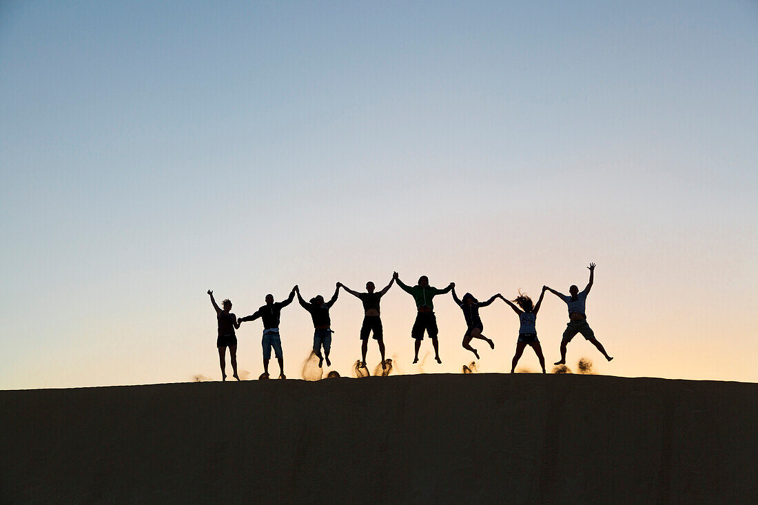 Silhouette of people jumping on a sand dune