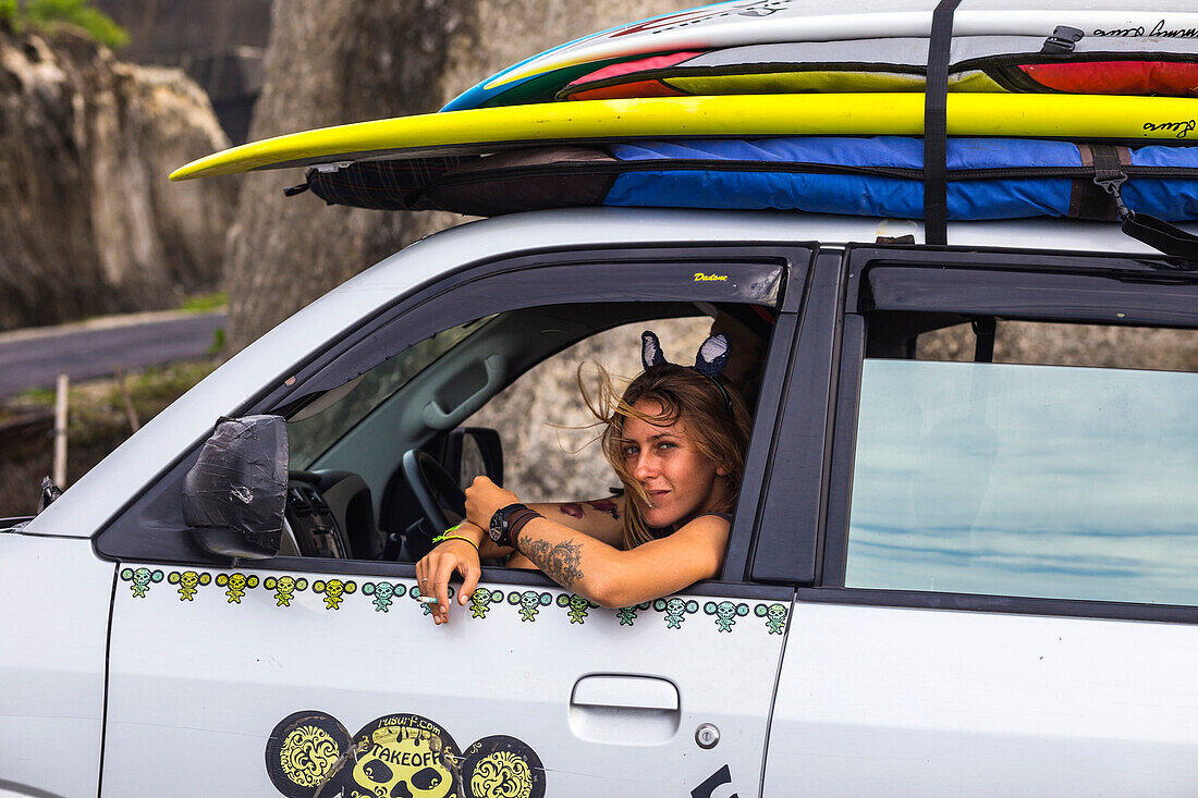 Teenage girl sitting in car with surfboard.