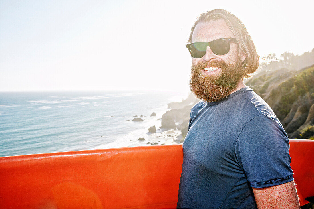 Caucasian man holding surfboard on coastal cliff
