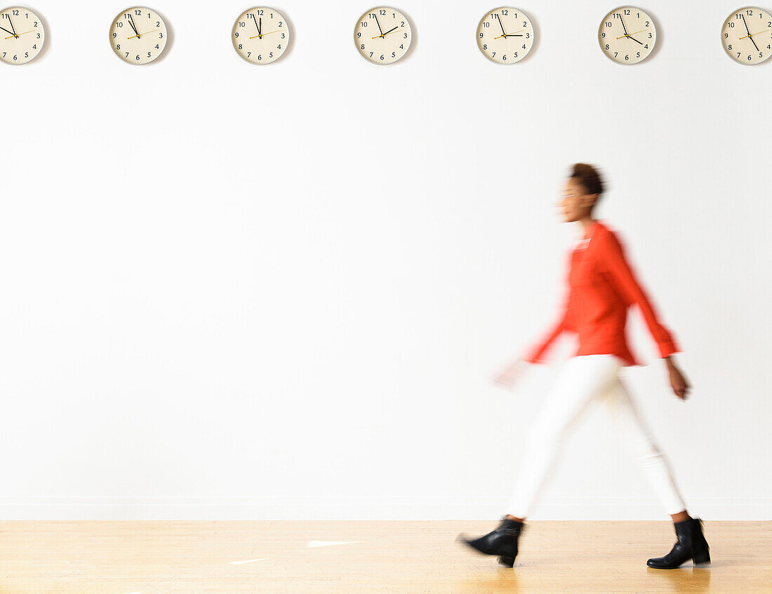 Mixed race businesswoman walking under clocks