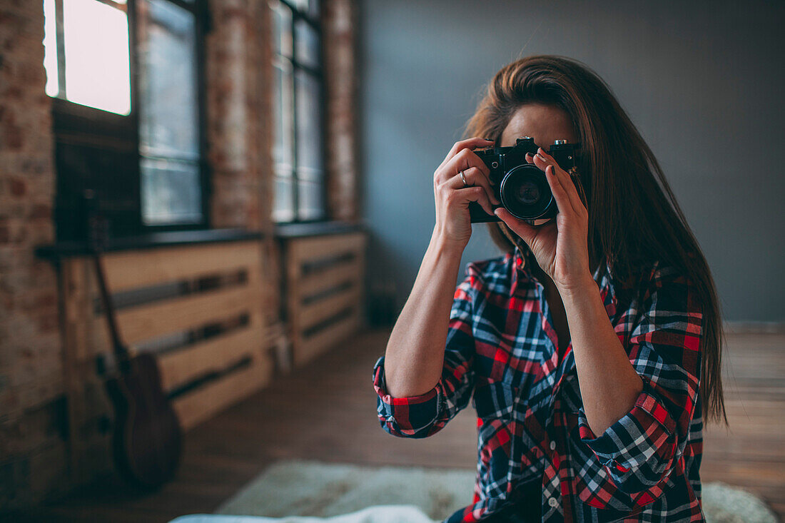 Woman photographing through SLR camera in bedroom at home