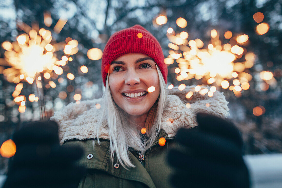 Happy woman holding sparklers during winter
