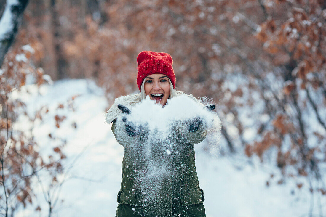 Portrait of happy young woman playing with snow