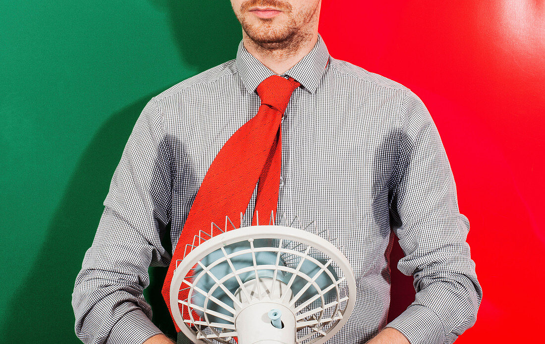 Midsection of businessman with sweaty armpits holding fan against colored background