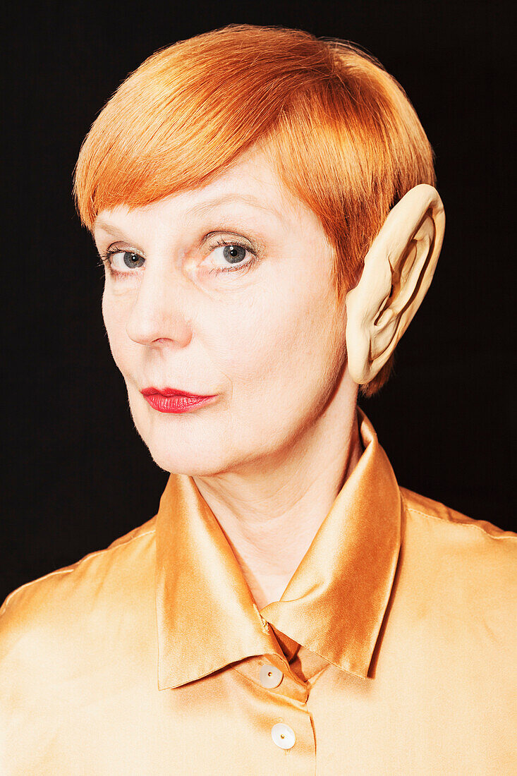 Portrait of confident mature woman wearing enormous monster ear against black background