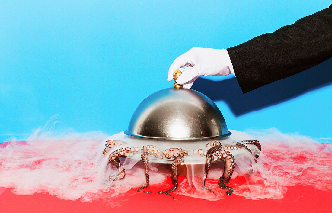 Cropped image of waiter lifting domed tray against blue background
