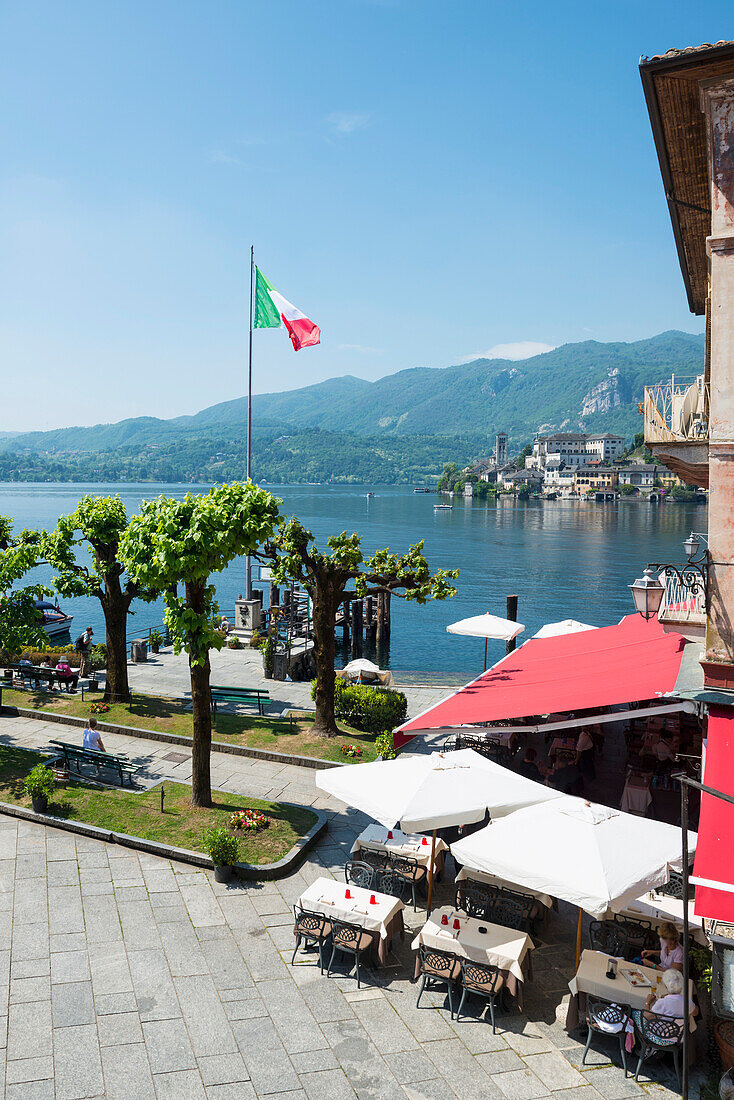 Flag of Italy flying at the waterfront beside a restaurant patio on Lake Orta Orta, Piedmont, Italy