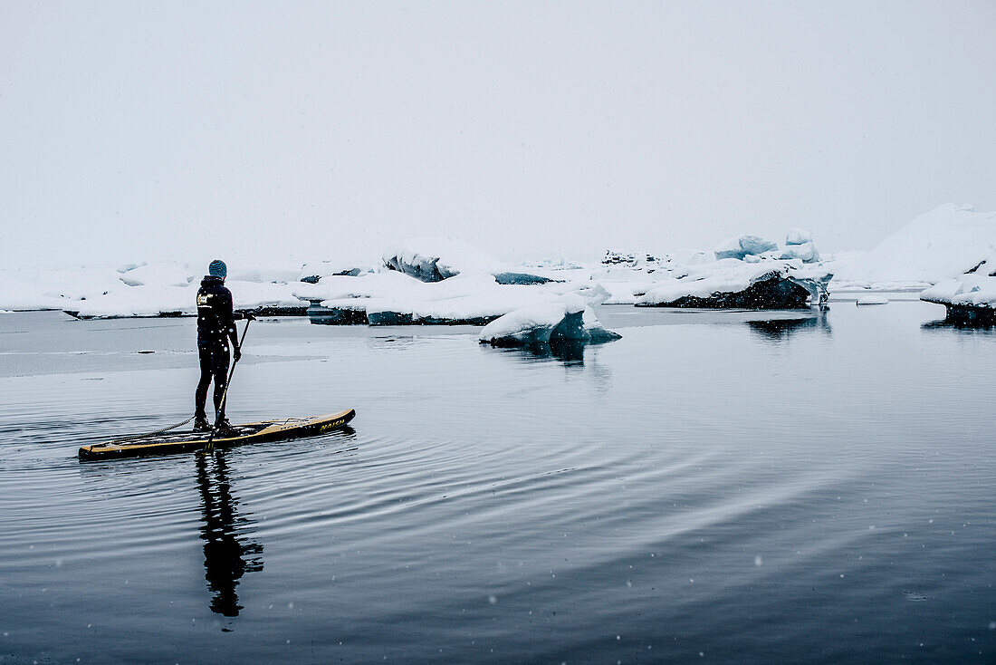 Man stand up paddling on glacial lake Jokulsarlonat at Vatnajokul, Iceland