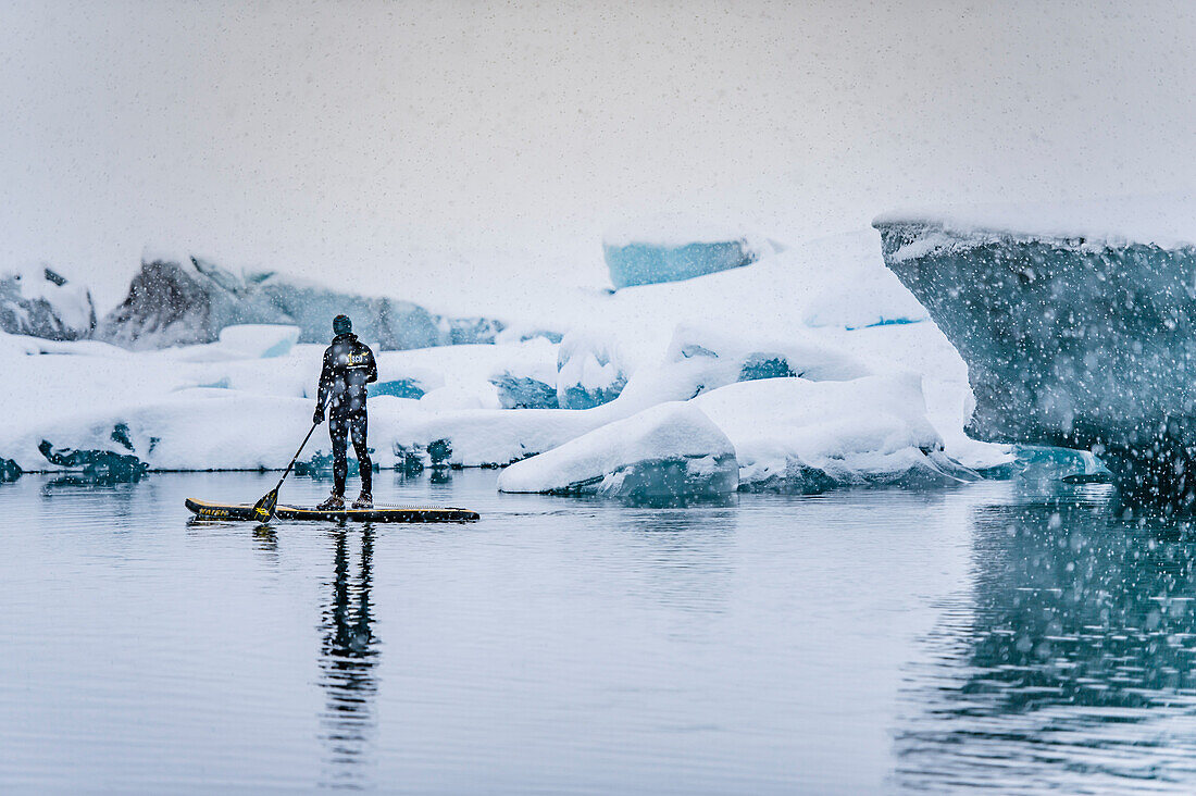 Man stand up paddling on a glacier lagoon Jokulsarlon at Vatnajokul, Iceland