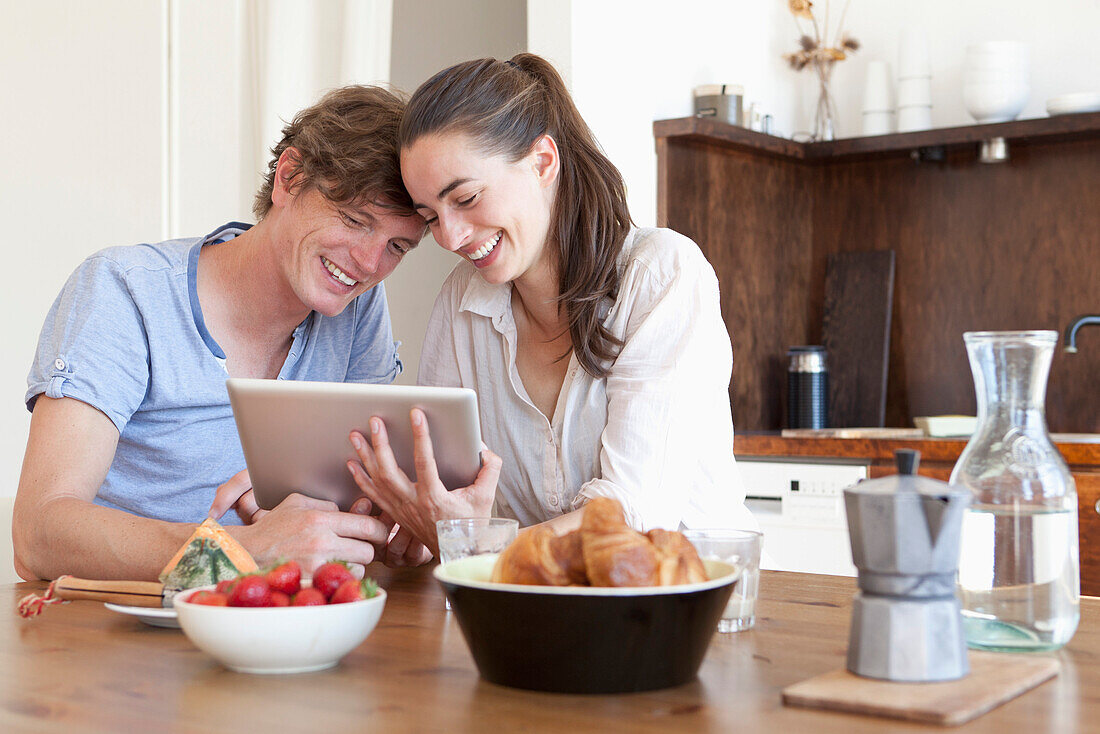 Young couple sitting at dining table, using digital tablet