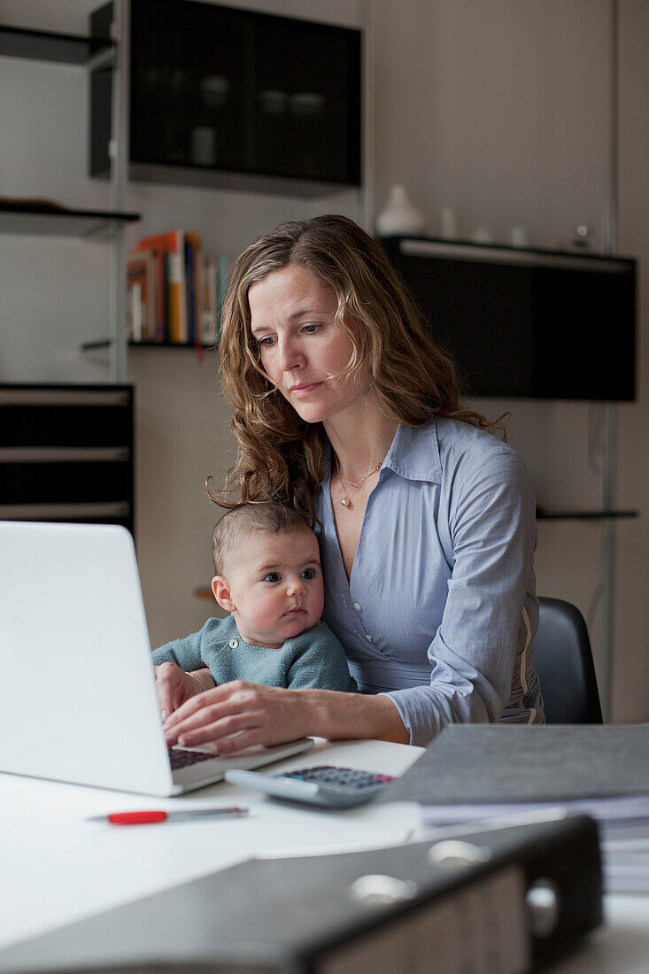 Woman using laptop while sitting with baby girl at home