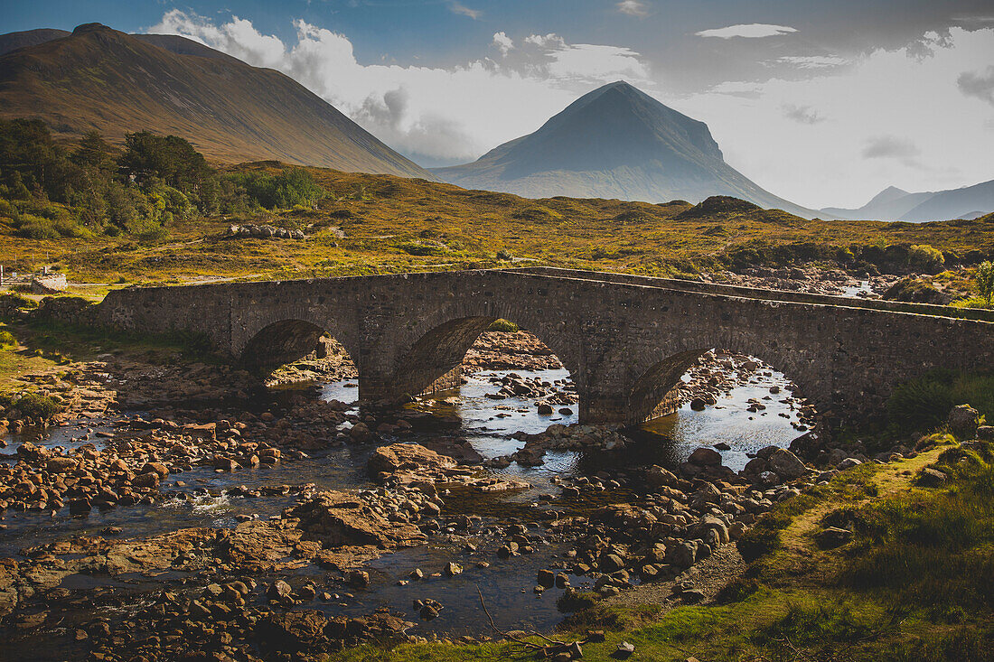 Abandoned arch bridge over stream against mountains