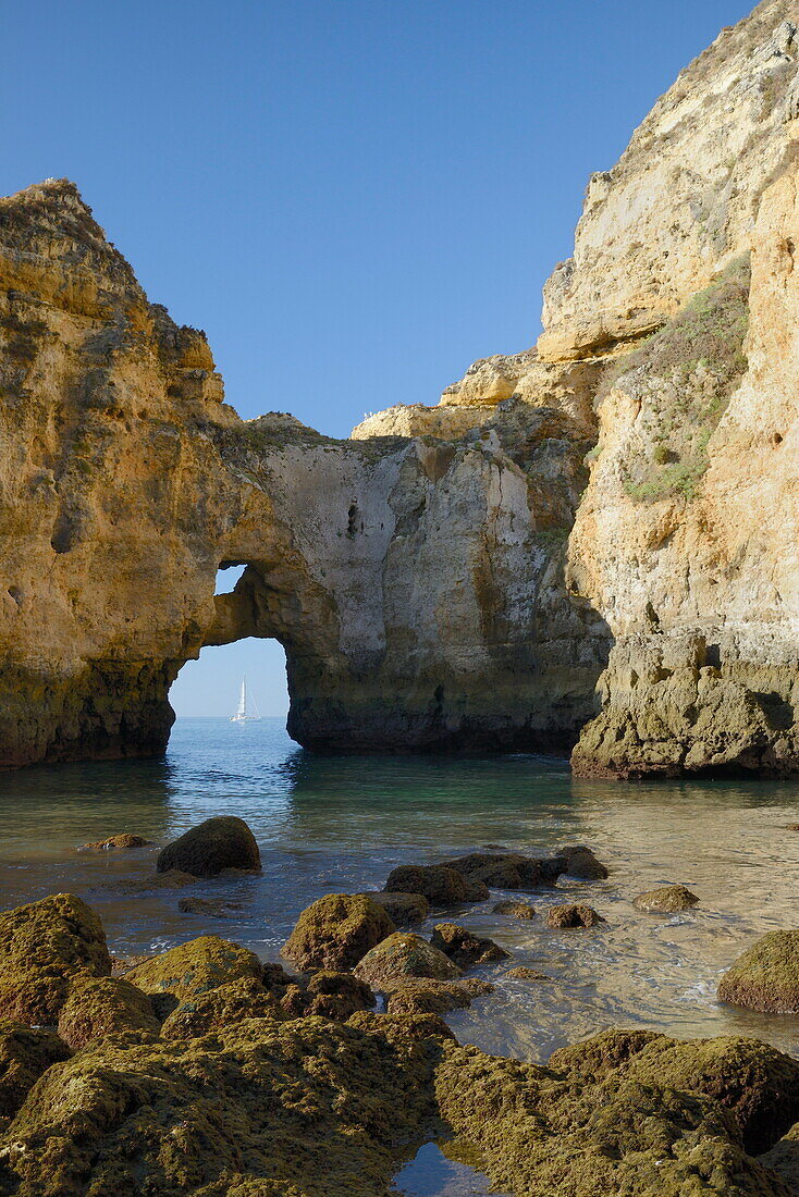 Weathered sandstone cliffs and sea stacks at Ponta da Piedade in morning light with a yacht framed by a rock arch, Lagos, Algarve, Portugal, Europe