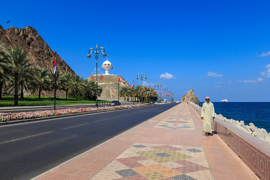 Man wearing dishdasha walks along Mutrah Corniche with national flags, flower beds and Giant Incense Burner, Muscat, Oman, Middle East