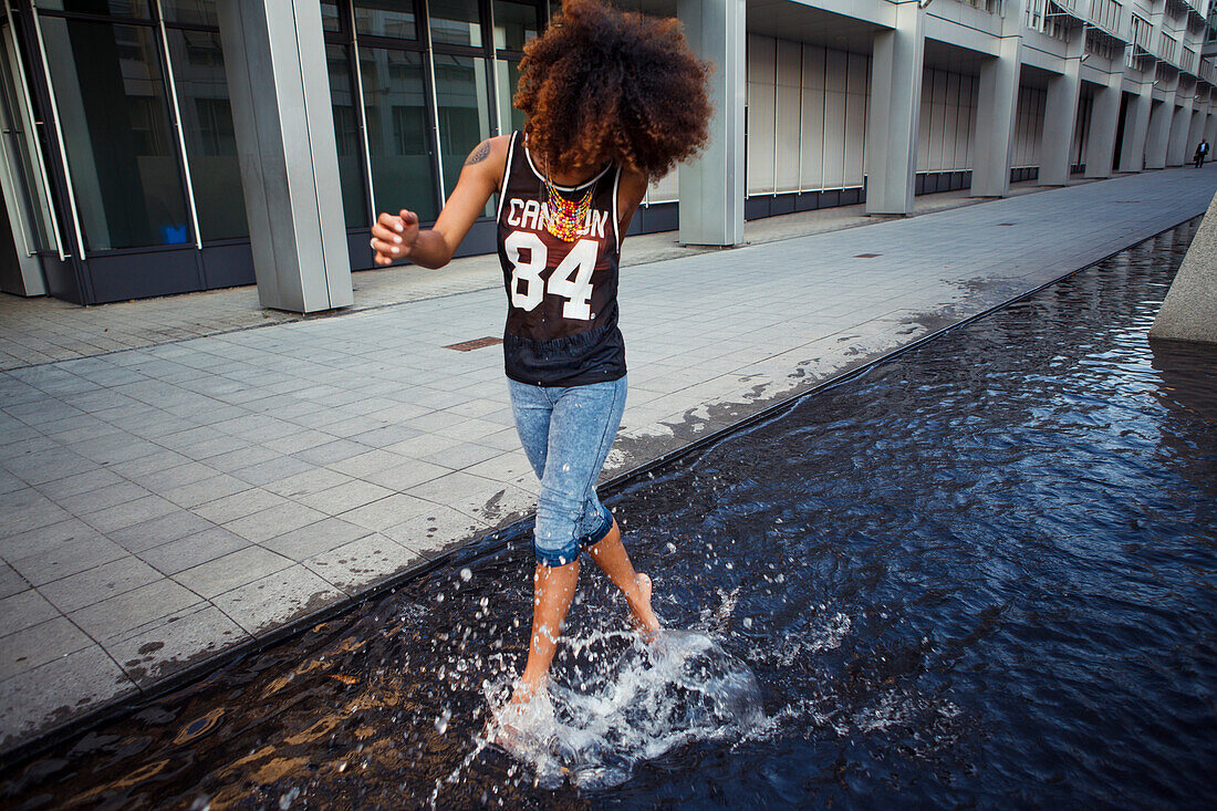 Sportliche, junge afroamerikanische Frau in urbaner Szene beim Laufen durch Wasserbrunnen, München, Bayern, Deutschland
