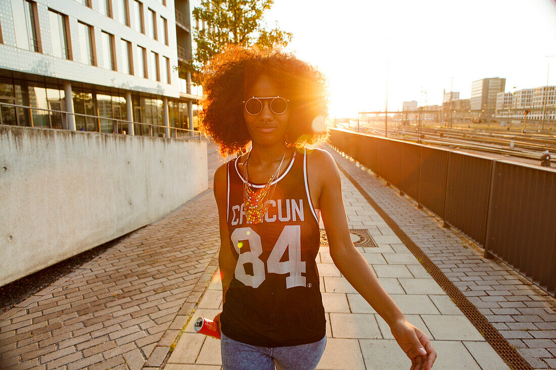 Coole, sportliche junge afroamerikanische Frau geht im Gegenlicht in moderner urbaner Szenerie, München, Bayern, Deutschland