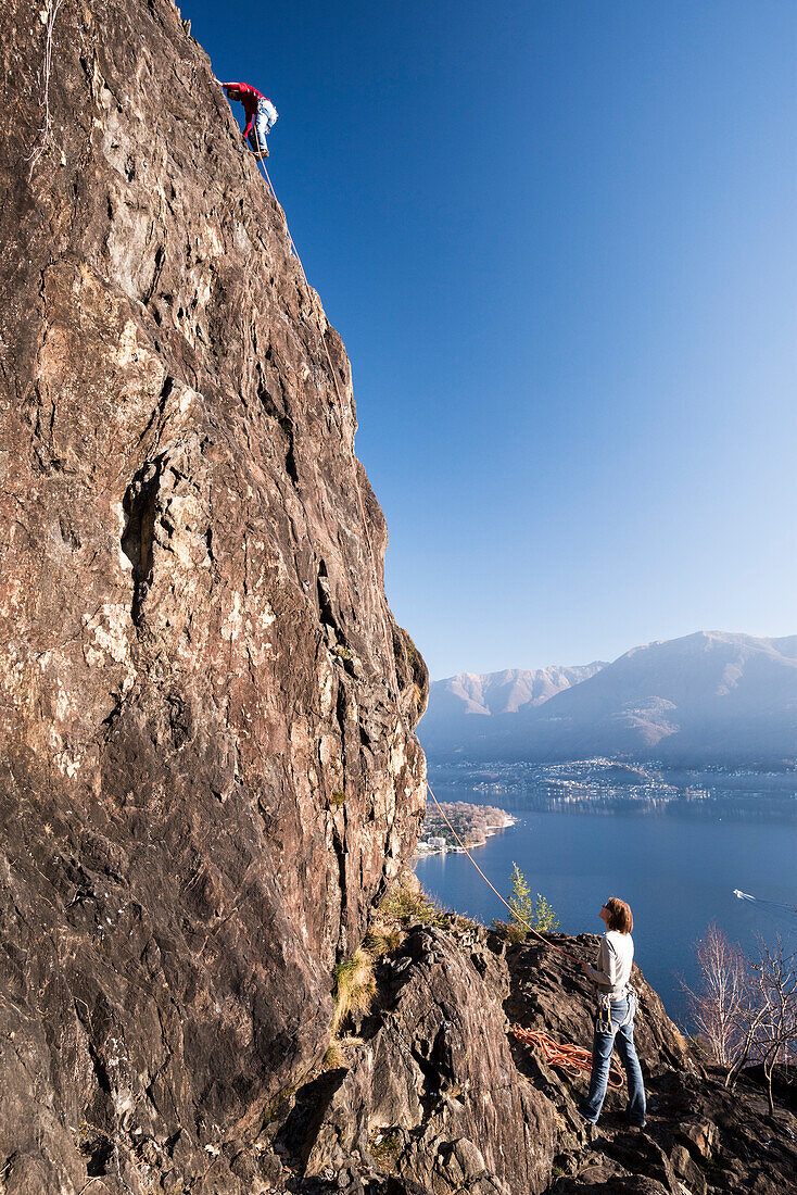 A couple is climbing on the crags of Baladrum above Ascona, in the background Lake Maggiore, canton of Ticino, Switzerland