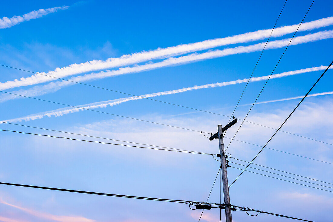 Typical open land phone and power supply lines on wooden posts with condensation trail in the blue sky, Toronto, Canada