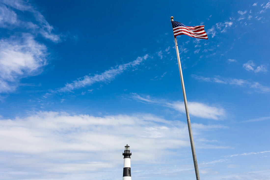 Black white striped lighthouse on the offshore island chain Outerbanks with the American national flag, Nags Head, Outer Banks, North Carolina, USA