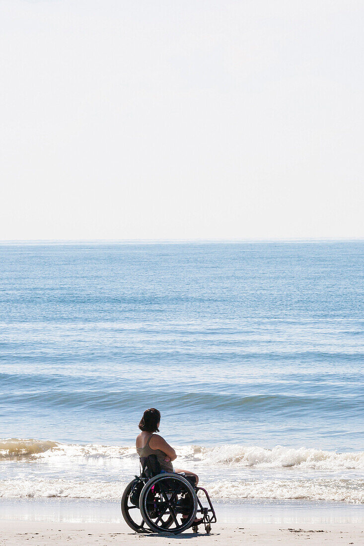Eine Frau im Rollstuhl am Strand schaut auf den Atlantik, Charleston, South Carolina, USA