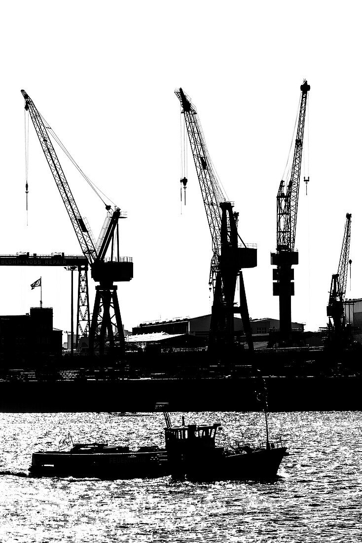 Silhouette of a launch on the Elbe in front of shipyard cranes of Blohm and Voss, Hamburg, Germany