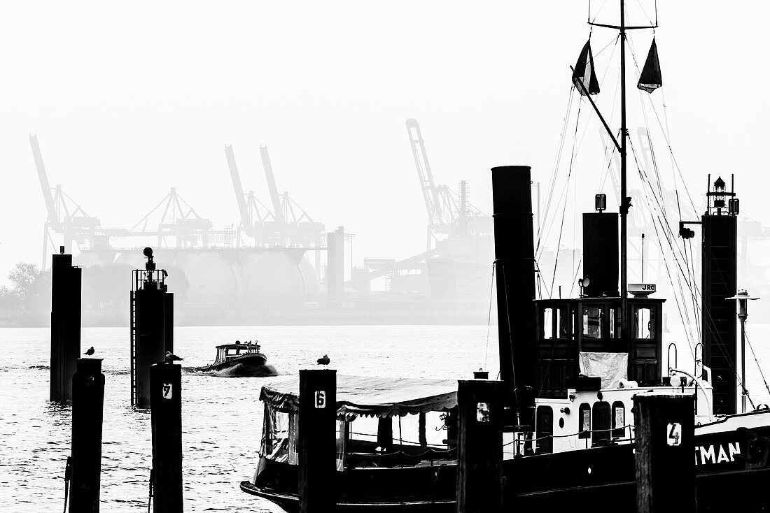 View from  the museum harbour with an old steamboat at the Elbe with a lauch in front of the industrial scenery with container cranes, Oevelgönne, Hamburg, Germany